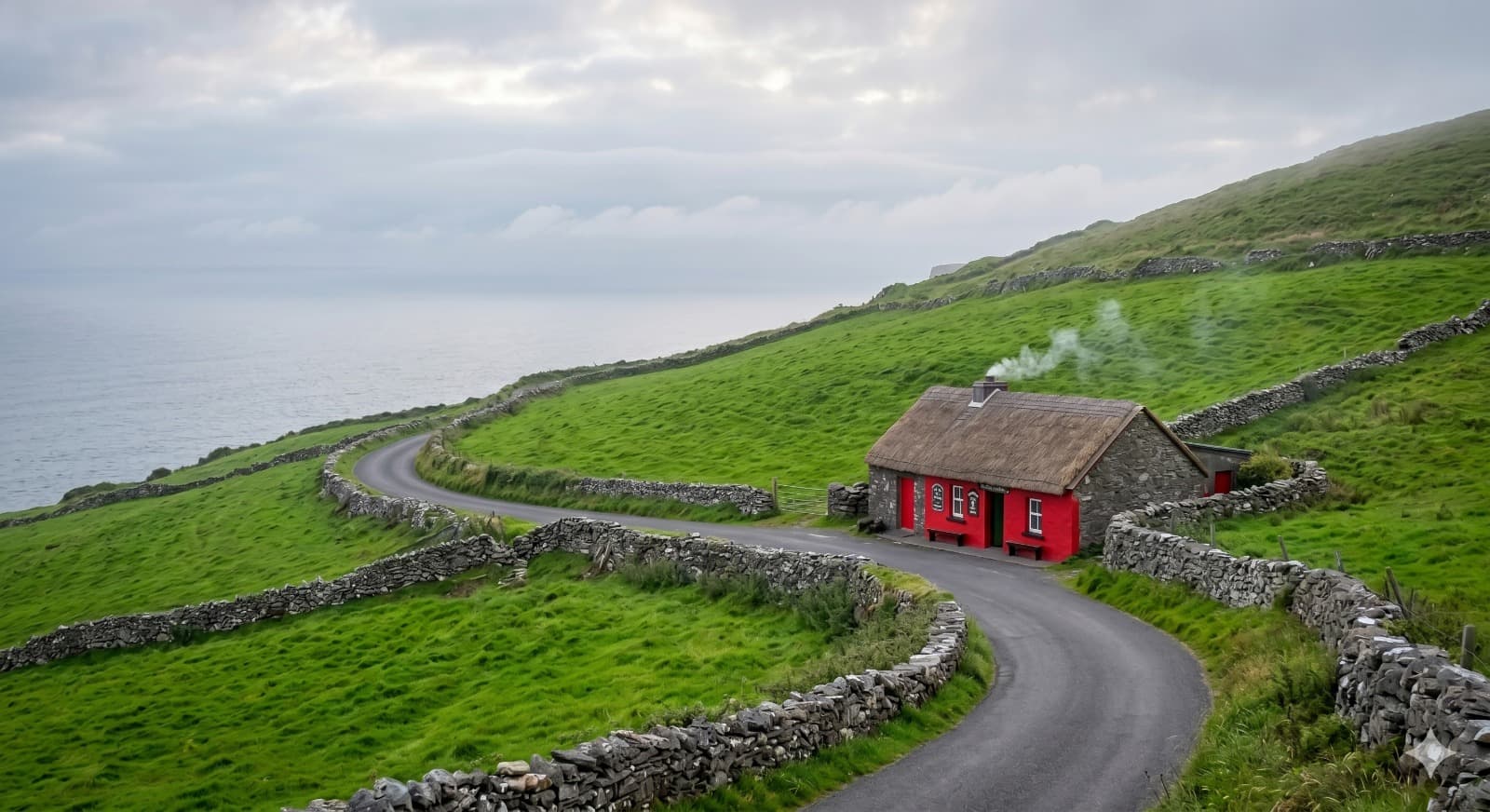 A red cottage on a winding Irish coastal road surrounded by green hills